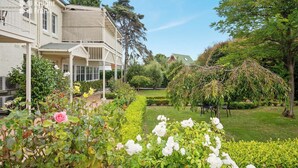 A large, two-story building with a covered porch and a well-maintained garden with various plants and flowers. - Clydesdale Manor (Sandy Bay)