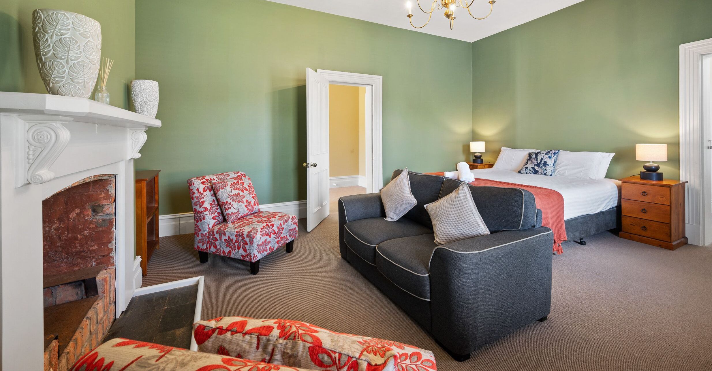 A bedroom with a bed, a sofa, a chair, a fireplace, and a nightstand with lamps.