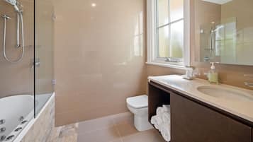 A modern bathroom with a glass-enclosed shower, a white bathtub, a toilet, and a vanity with a mirror.
