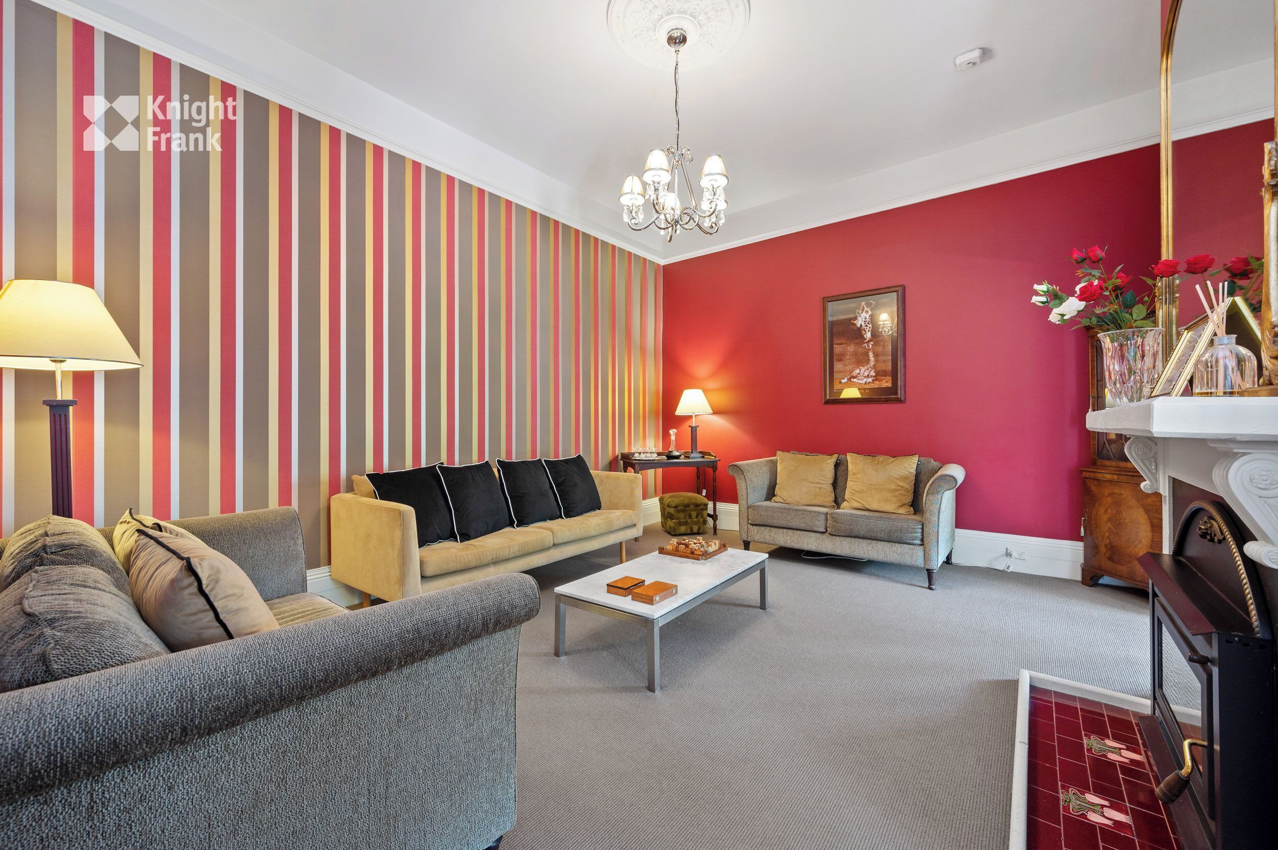 A living room with striped wallpaper, a chandelier, and two sofas.
