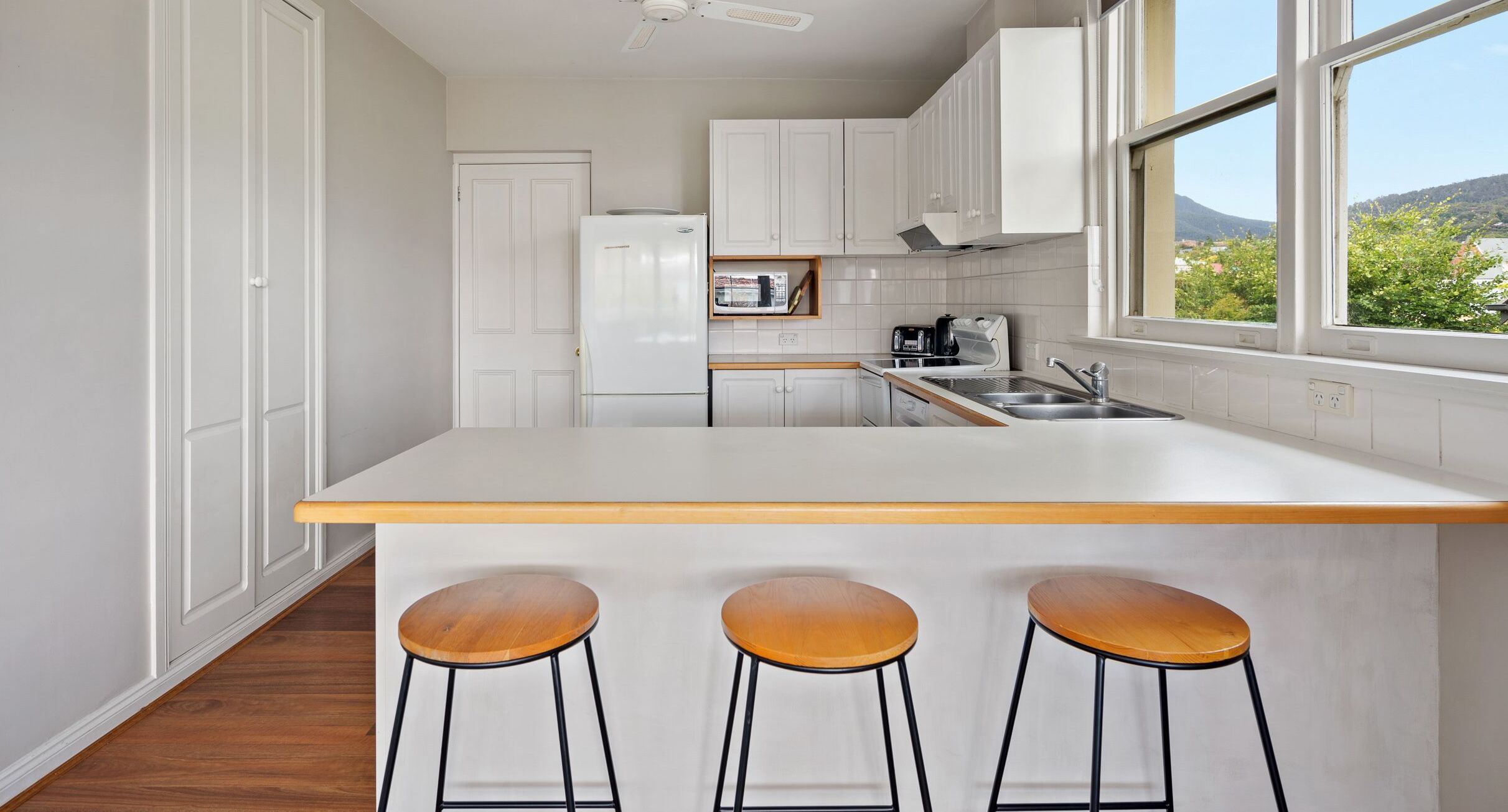 Une cuisine moderne avec des meubles blancs, un plan de travail en bois et trois tabourets.