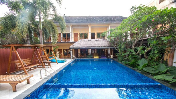 A swimming pool with a tiled deck, wooden lounge chairs, and a covered seating area. - Central Inn (Senggigi)