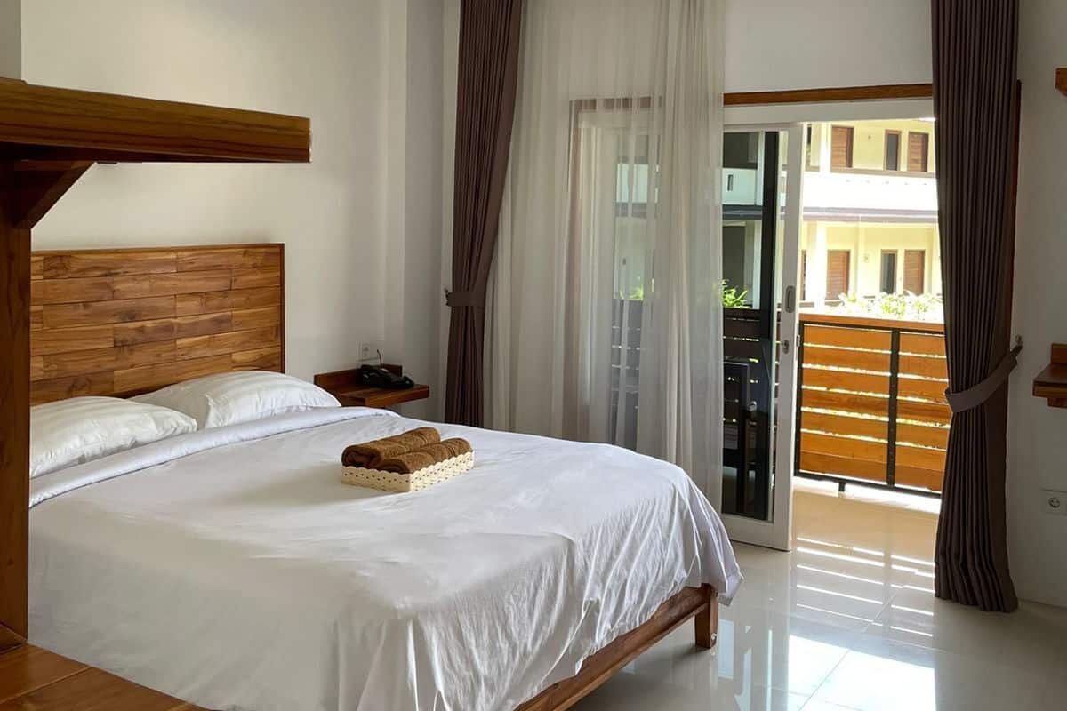 A bedroom with a wooden headboard, a large bed, a bedside table, and a view of a building through a glass door.
