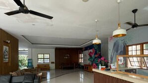 A spacious living area with a black sofa, a wooden reception desk, and a ceiling fan. - Central Inn (Senggigi)