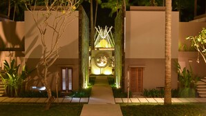Un bâtiment moderne doté d’une arche centrale illuminée, entouré d’une végétation luxuriante et de palmiers.