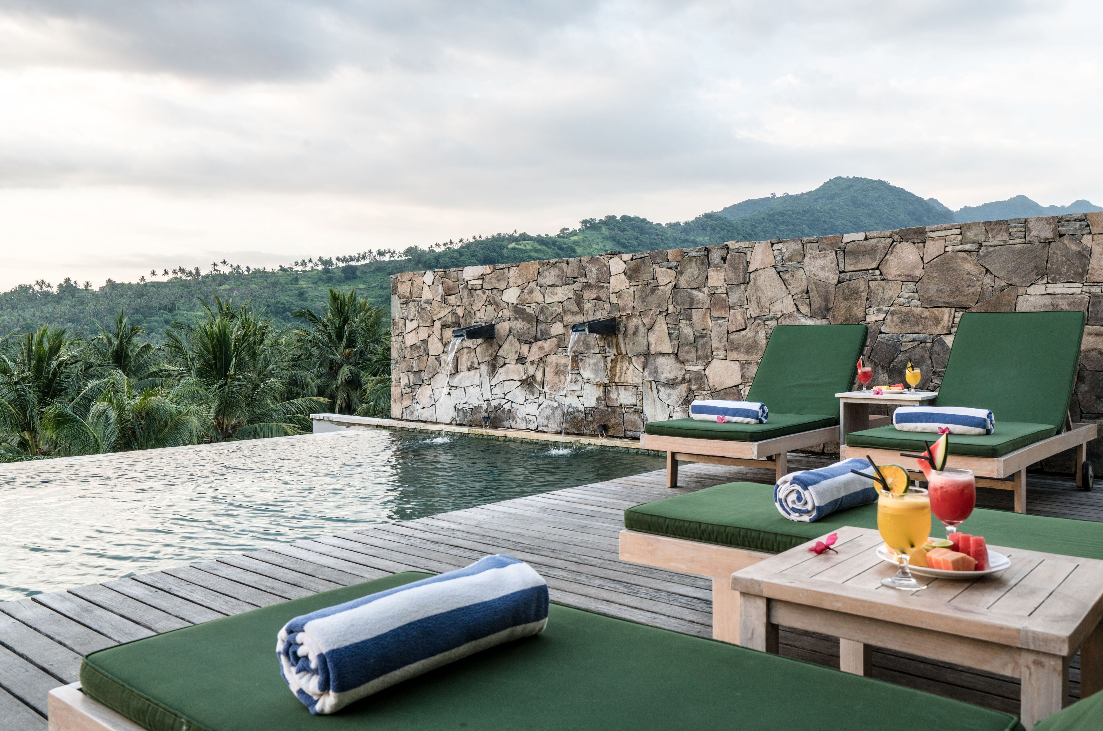A poolside area with lounge chairs, a table with drinks, and a stone wall.