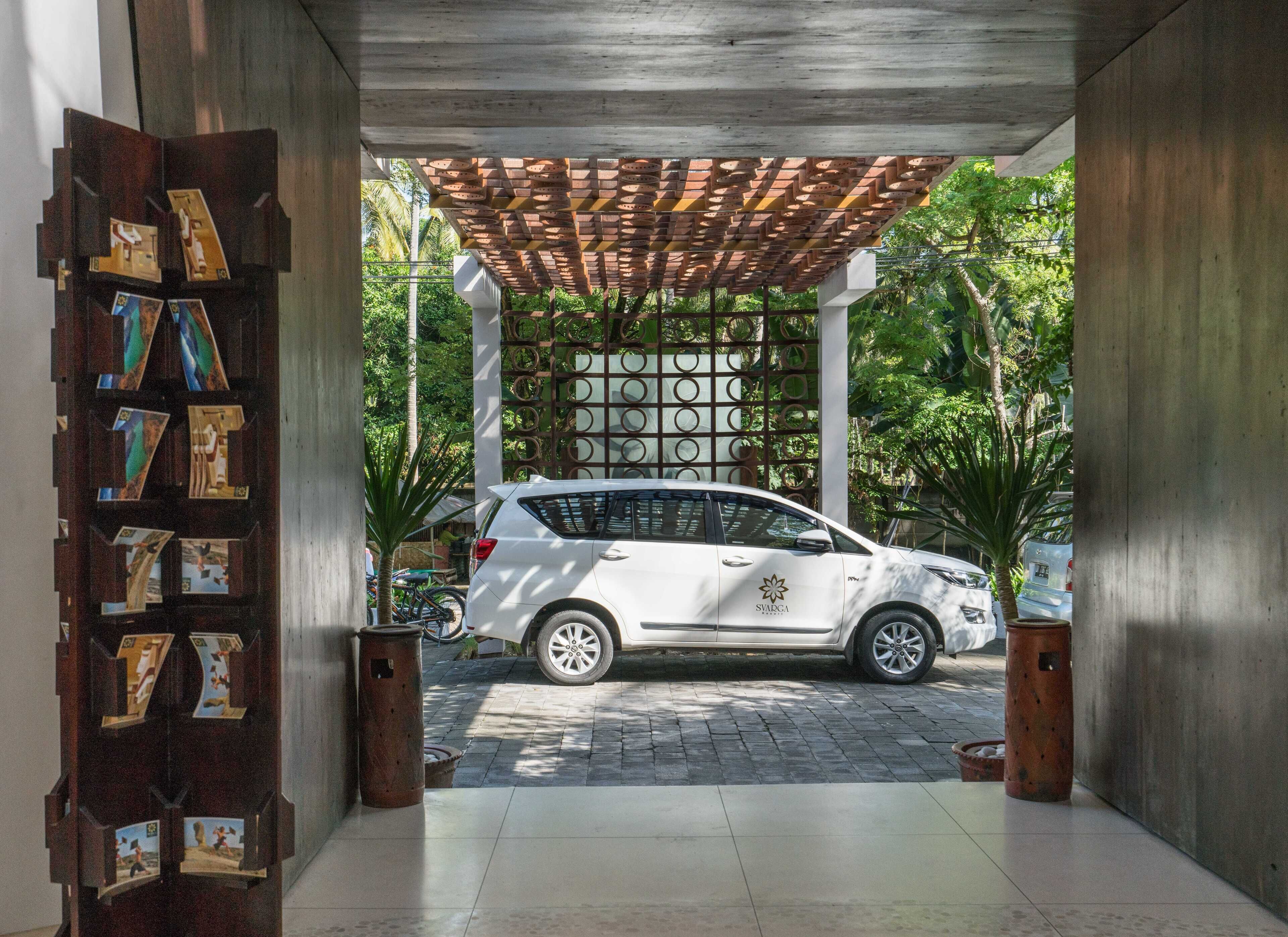 Un SUV blanco estacionado bajo una pérgola de madera con piso de baldosas y una pared decorativa con fotografías.