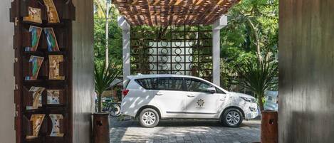 Un SUV blanco estacionado bajo una pérgola de madera con piso de baldosas y una pared decorativa con fotografías.
