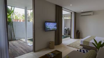A modern hotel room with a large sliding glass door leading to a pool area, a flat-screen TV mounted on the wall, a wooden coffee table, and a bed with patterned bedding.