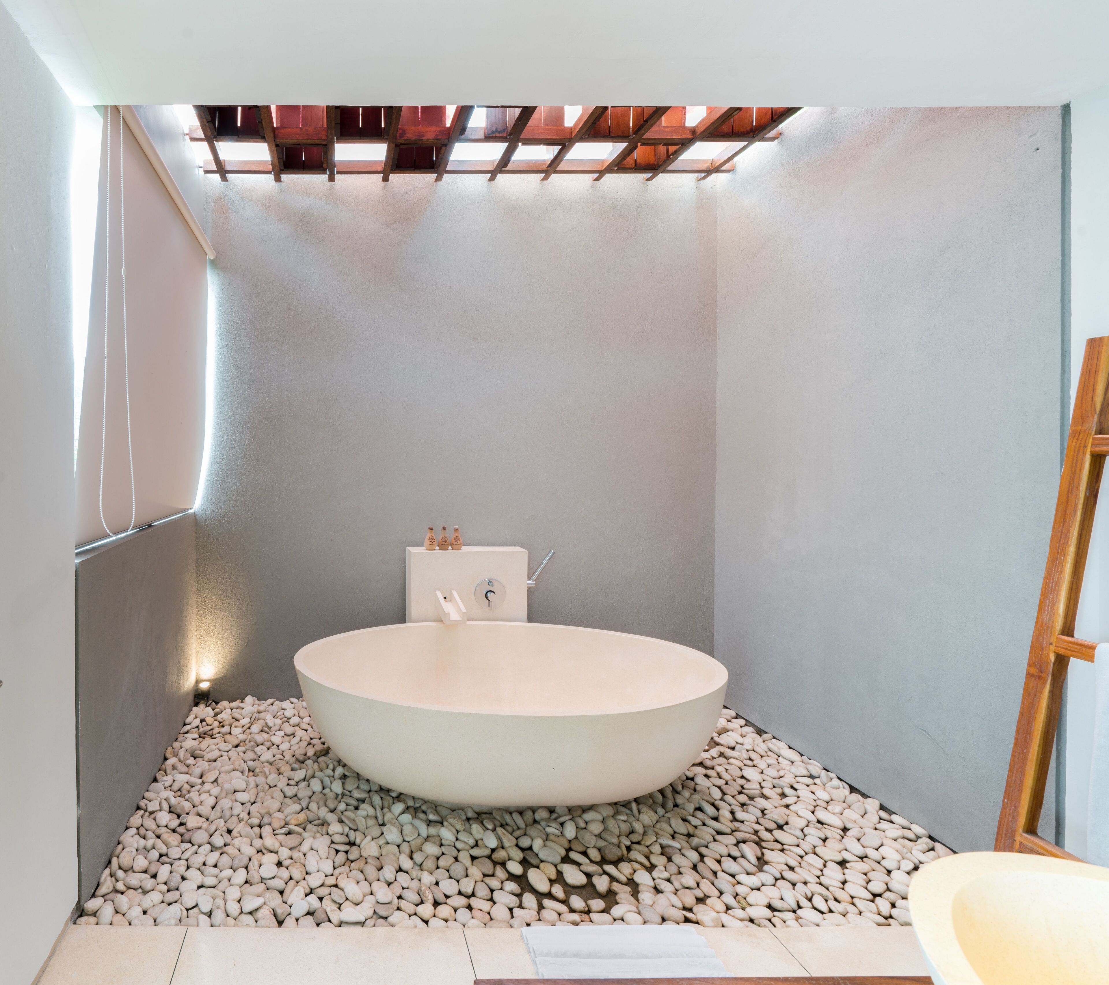 Ein modernes Badezimmer mit einer freistehenden Badewanne, einer Holzleiter und einem kleinen Regal mit Flaschen.