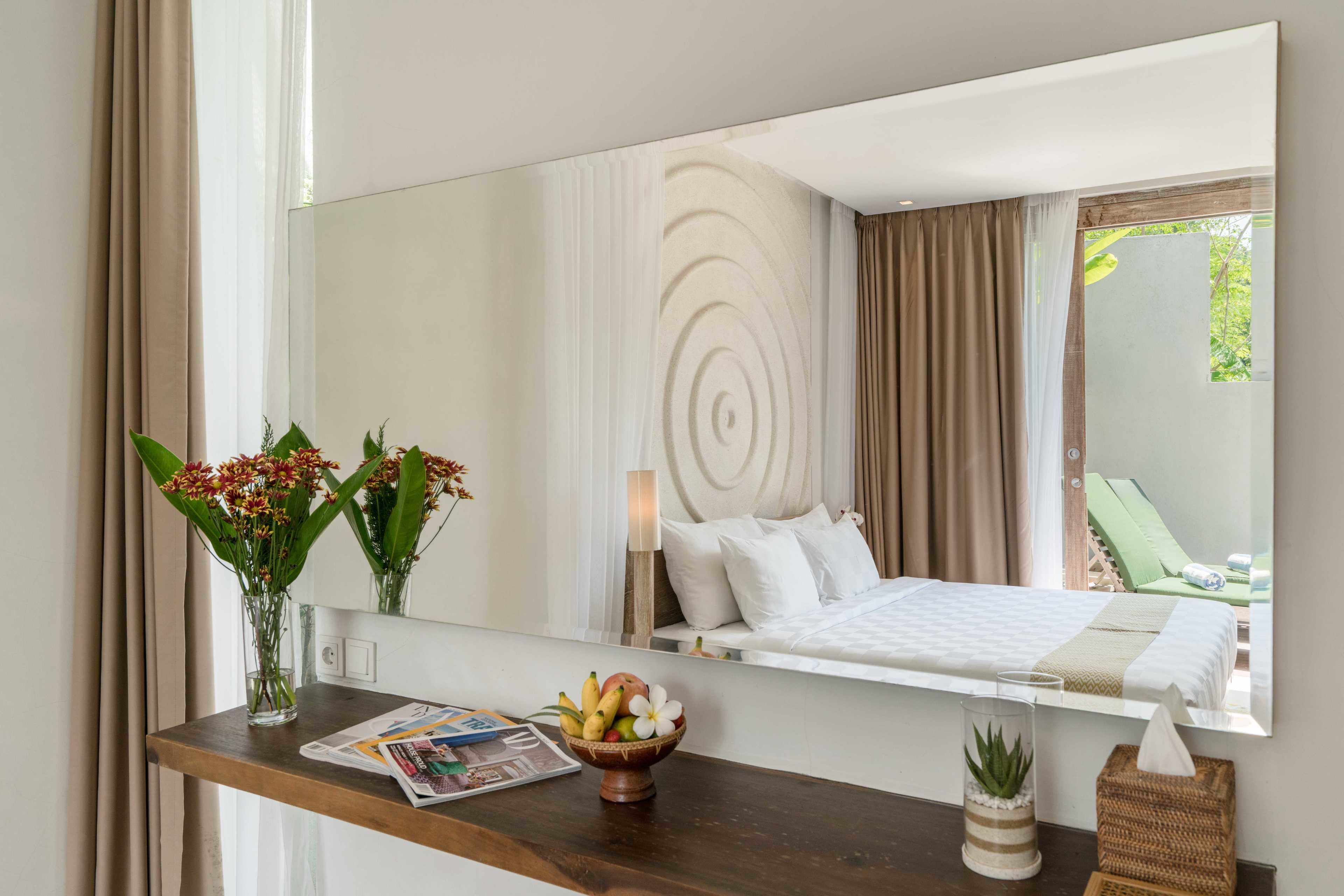Habitación de hotel con una cama, una mesita de noche con un florero, un frutero y un espejo que refleja la habitación.
