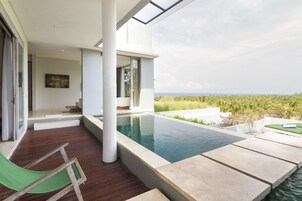 Zona de piscina exterior moderna con vista al océano, terraza de madera y una silla de descanso verde.