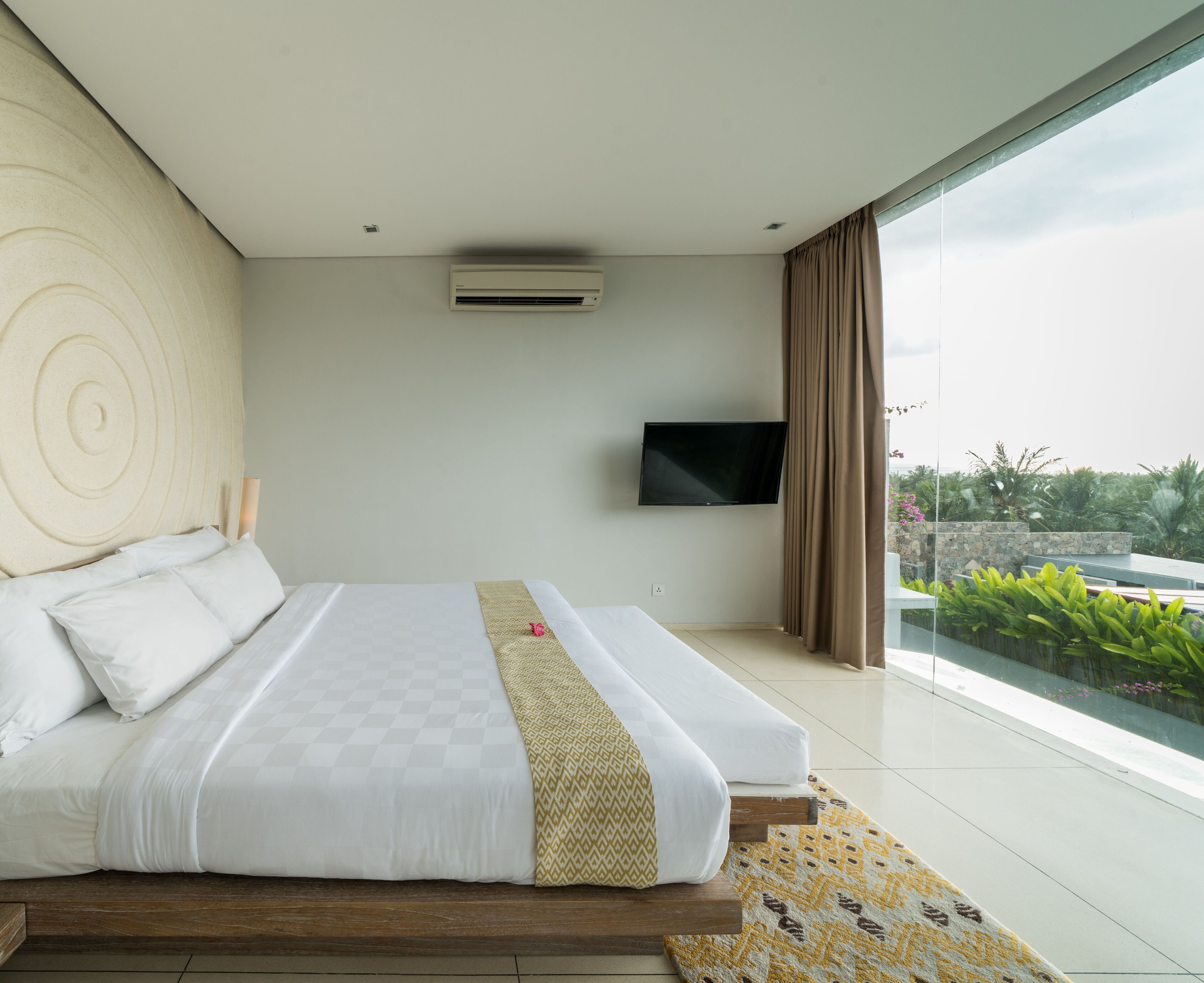 Une chambre d’hôtel moderne dotée d’un grand lit, d’un téléviseur à écran plat et offrant une vue sur la verdure grâce à une grande fenêtre.