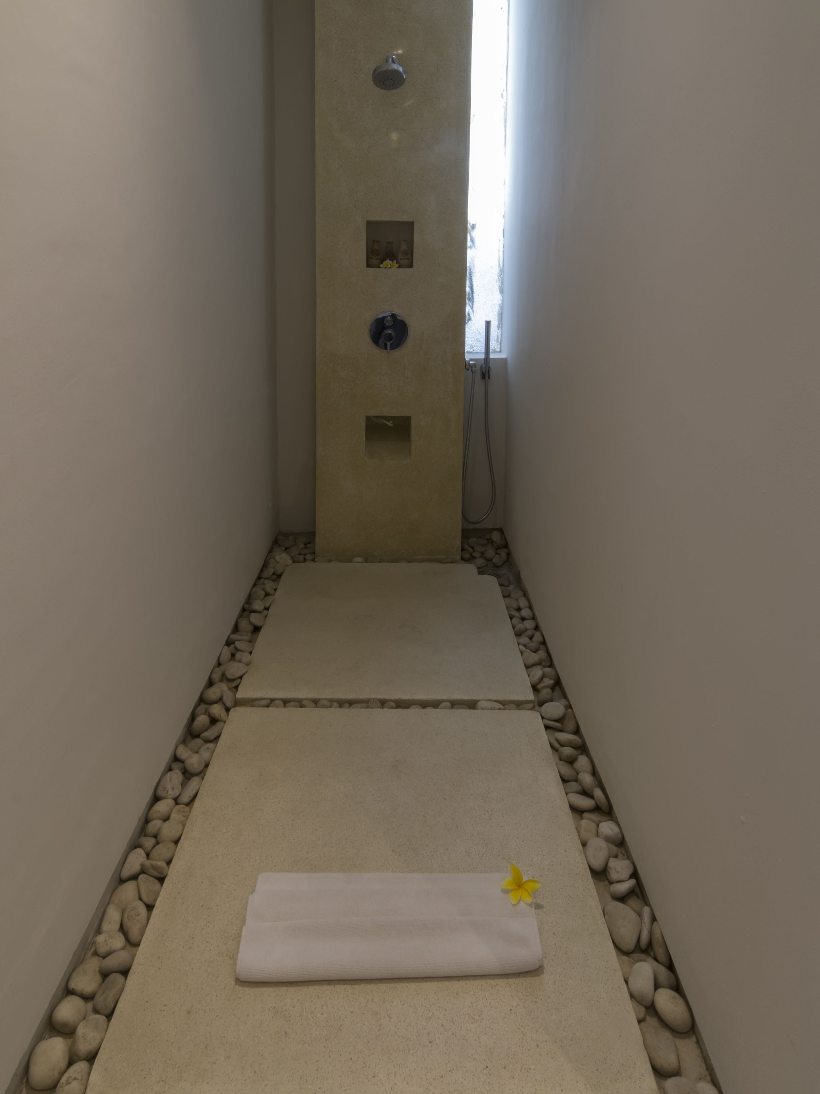 Un petit espace de douche carrelé, avec une serviette et une fleur jaune sur le sol.