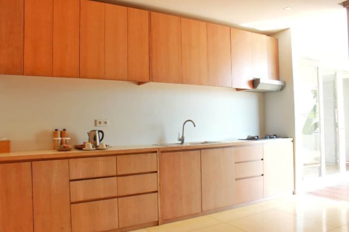 Una cocina moderna con armarios de madera, un lavamanos de acero inoxidable y una encimera con una tetera y frascos.