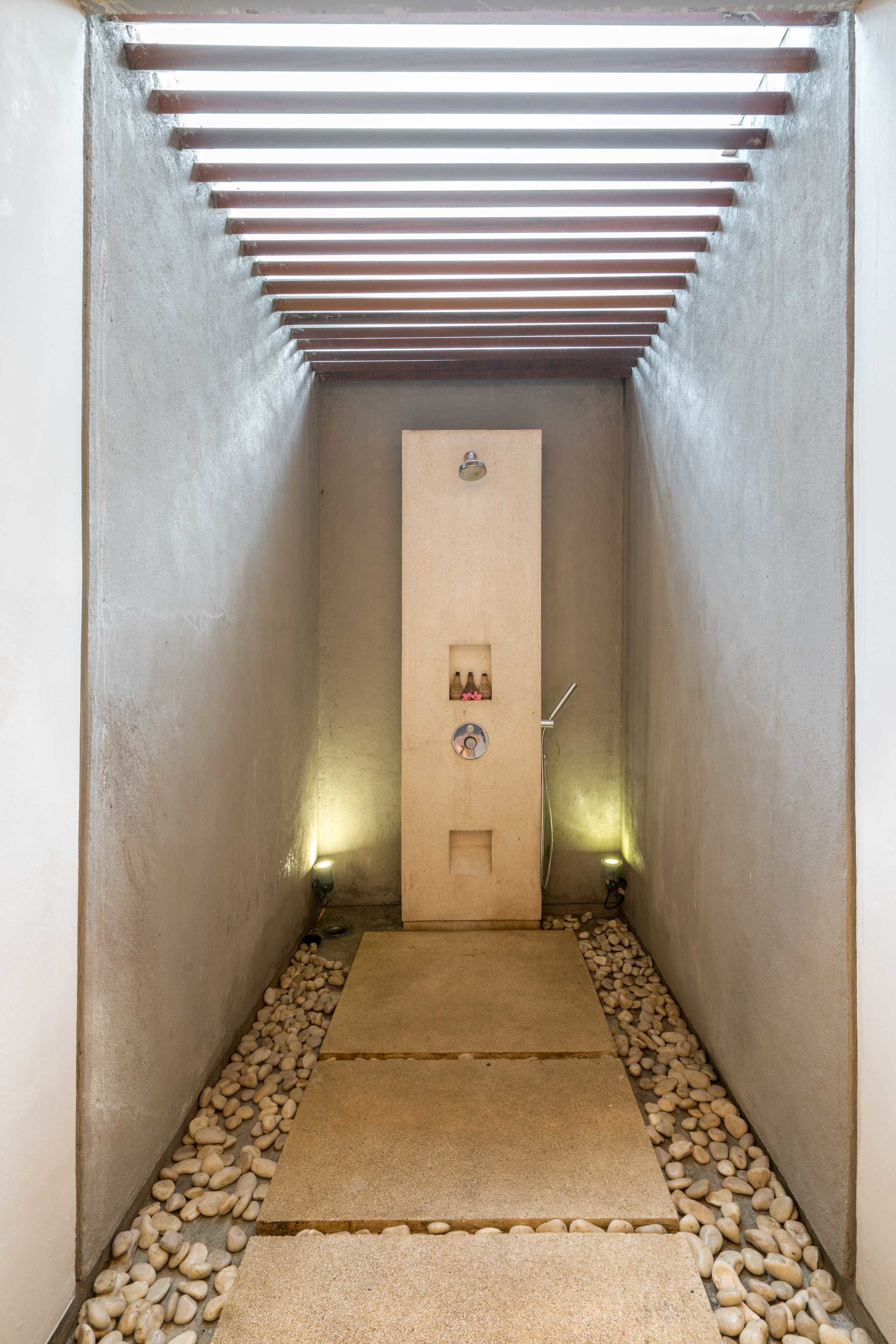 Un couloir étroit, avec une porte au fond, des petits cailloux sur le sol et une rambarde métallique au-dessus.