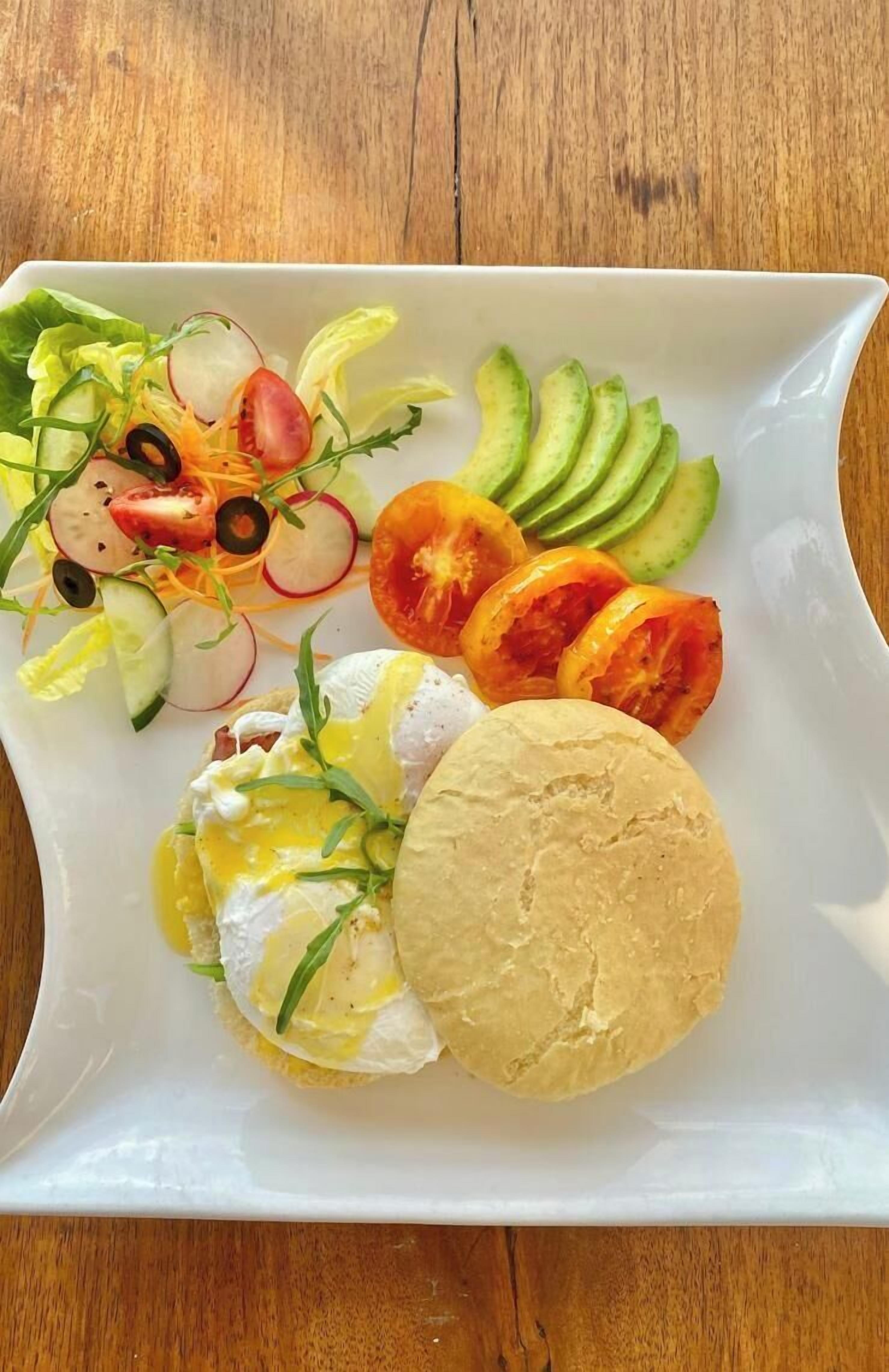 A white plate with poached eggs, avocado slices, and a salad on a wooden table.