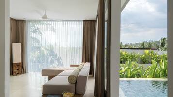 Relax in this serene living space with a comfortable sofa, coffee table, and stunning views of the lush landscape and pool.