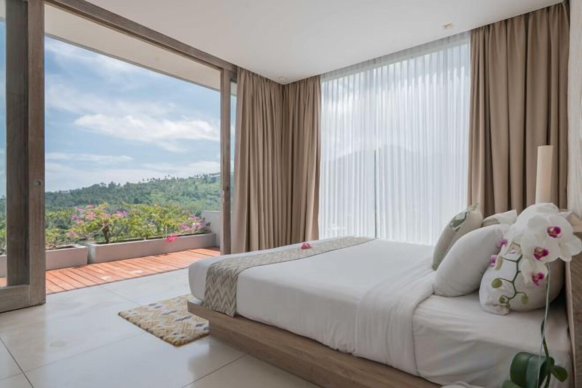 A bedroom with a large bed, a view of greenery, and a balcony.