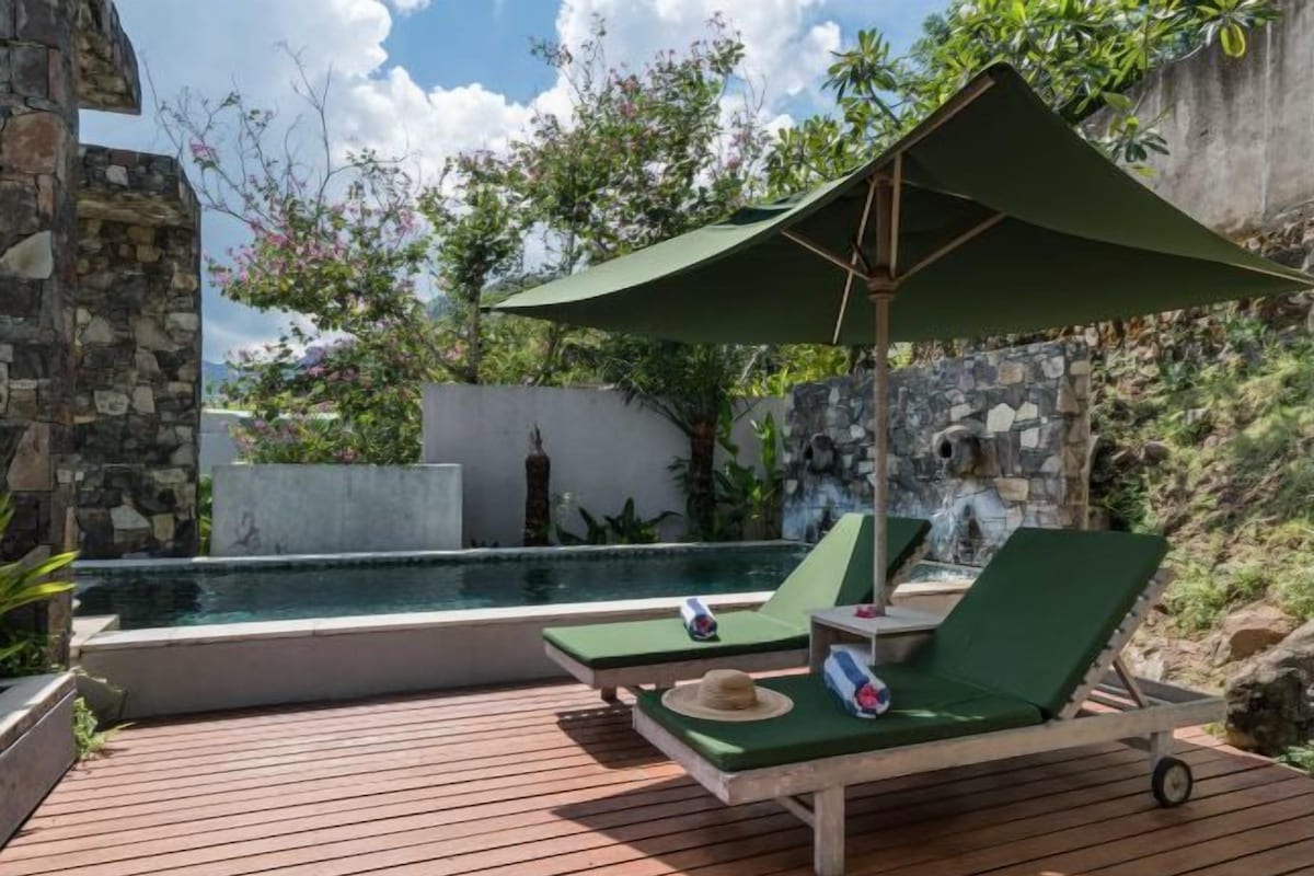 A poolside area with two lounge chairs, a small table, and a green umbrella.
