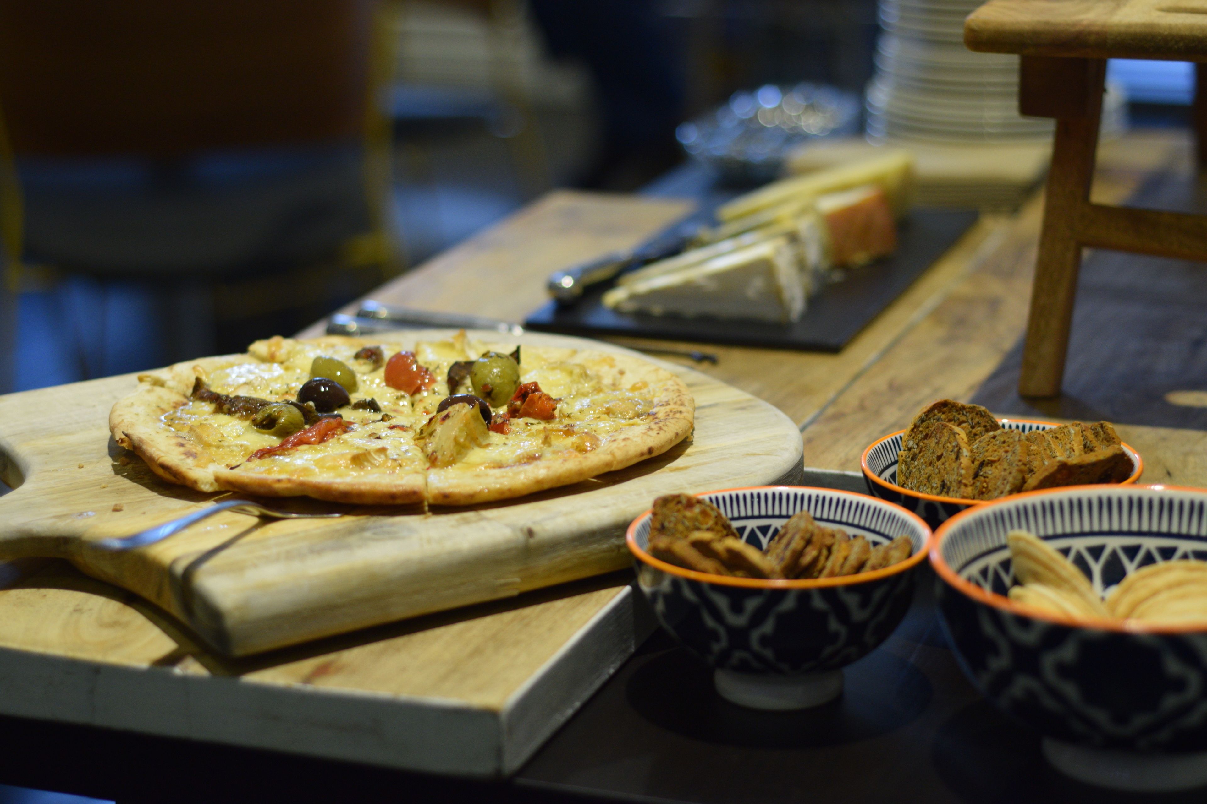 A wooden table with a pizza, bowls of bread, and a cheese board.