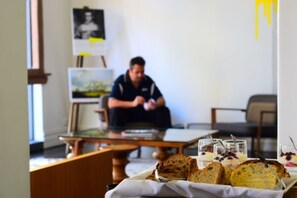 A room with a painting on the wall, a table with bread and glasses of a beverage, and a person sitting in the background.