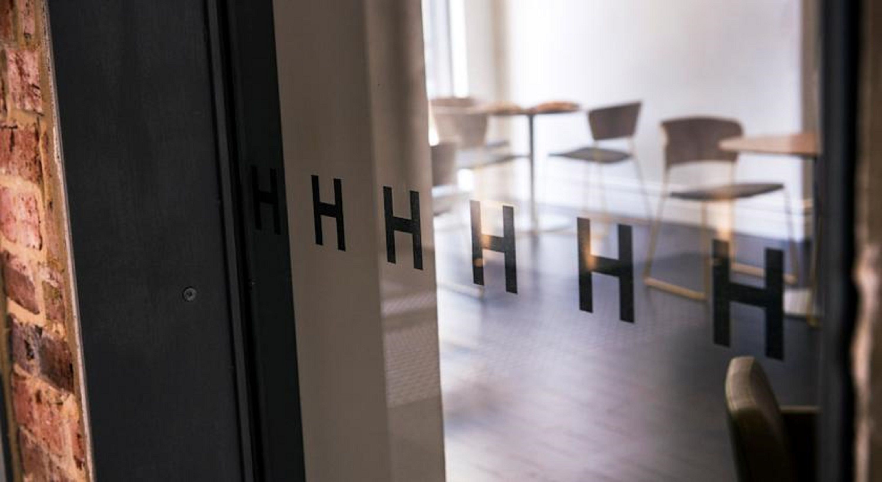 Una porta amb les lletres 'HHHHH', que condueix a una habitació de disseny modern i minimalista, amb una paret de maó i un sòl de fusta.