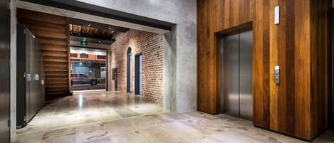 A modern elevator with a wooden panel design, a polished stone floor, and a brick wall in the background.