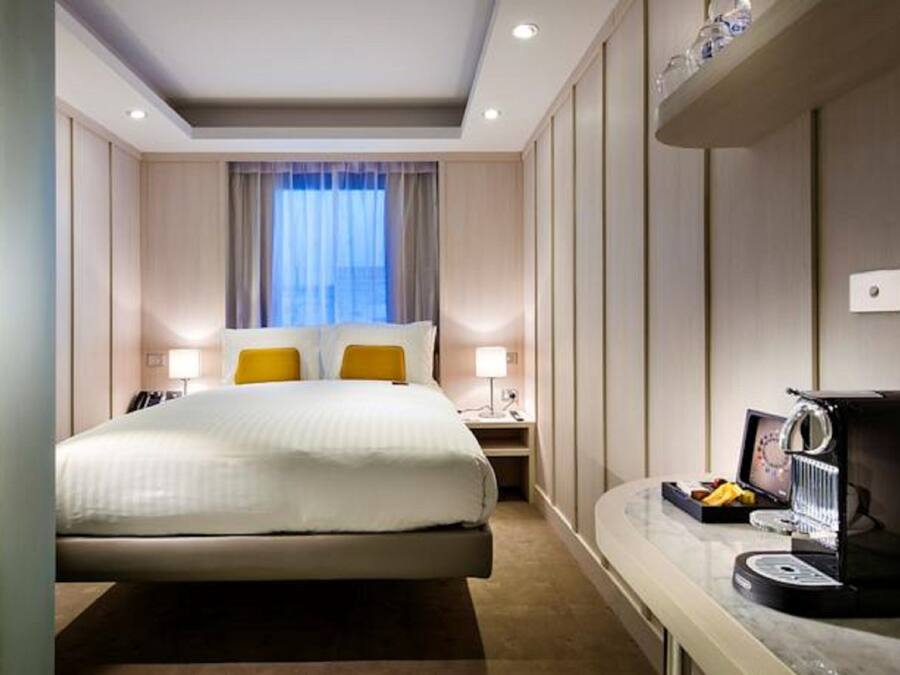 A hotel room with a bed, bedside lamps, a coffee machine, and a window with curtains.