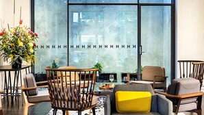 Un espacio lounge moderno con un ventanal grande, sillas de madera, una mesita con un vaso y una planta en maceta.