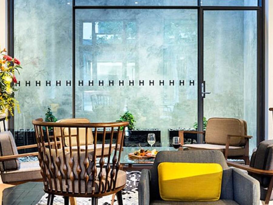 Un espacio lounge moderno con un ventanal grande, sillas de madera, una mesita con un vaso y una planta en maceta.