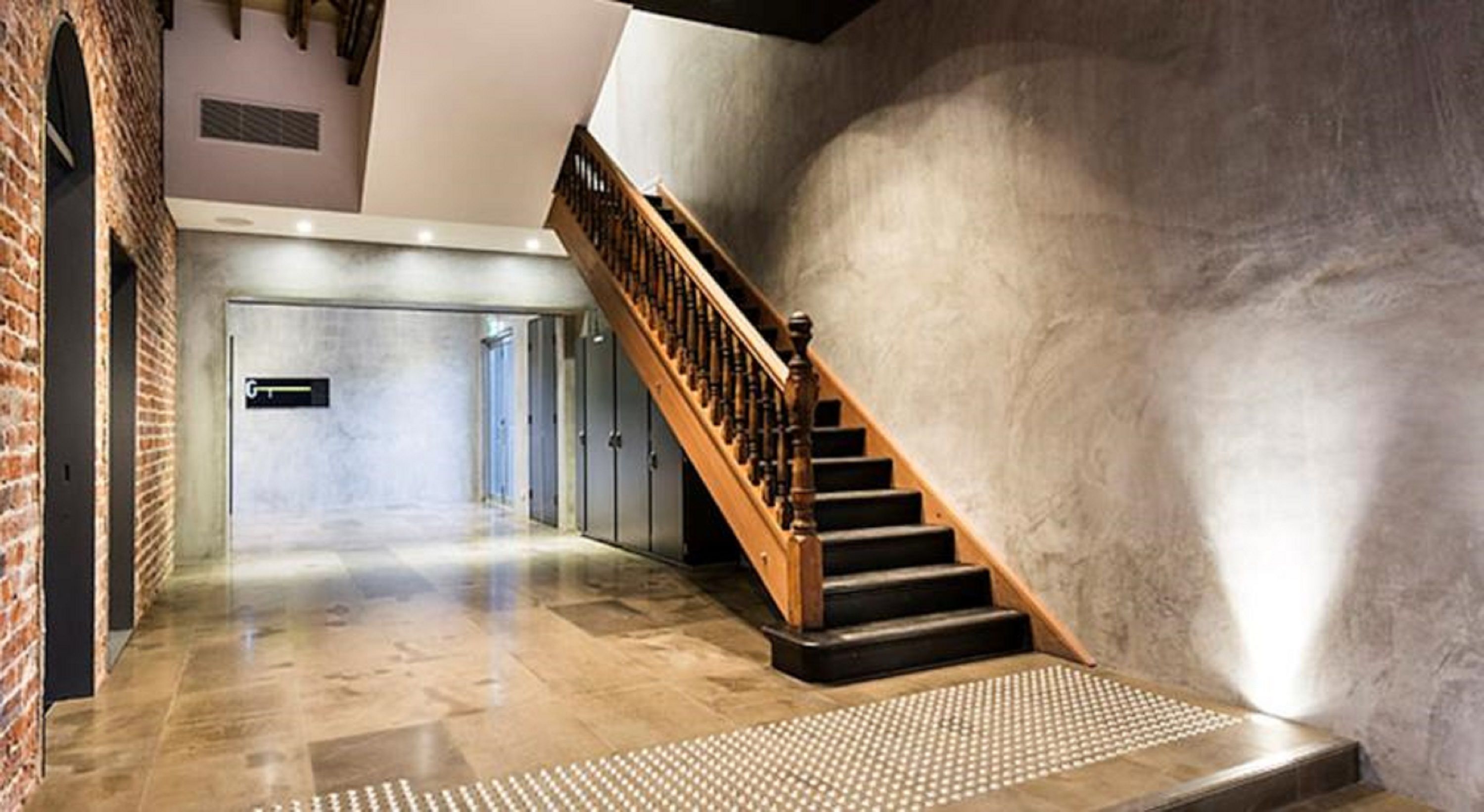 Un interior moderno con una escalera de madera, suelo de piedra pulida y pared de ladrillo.