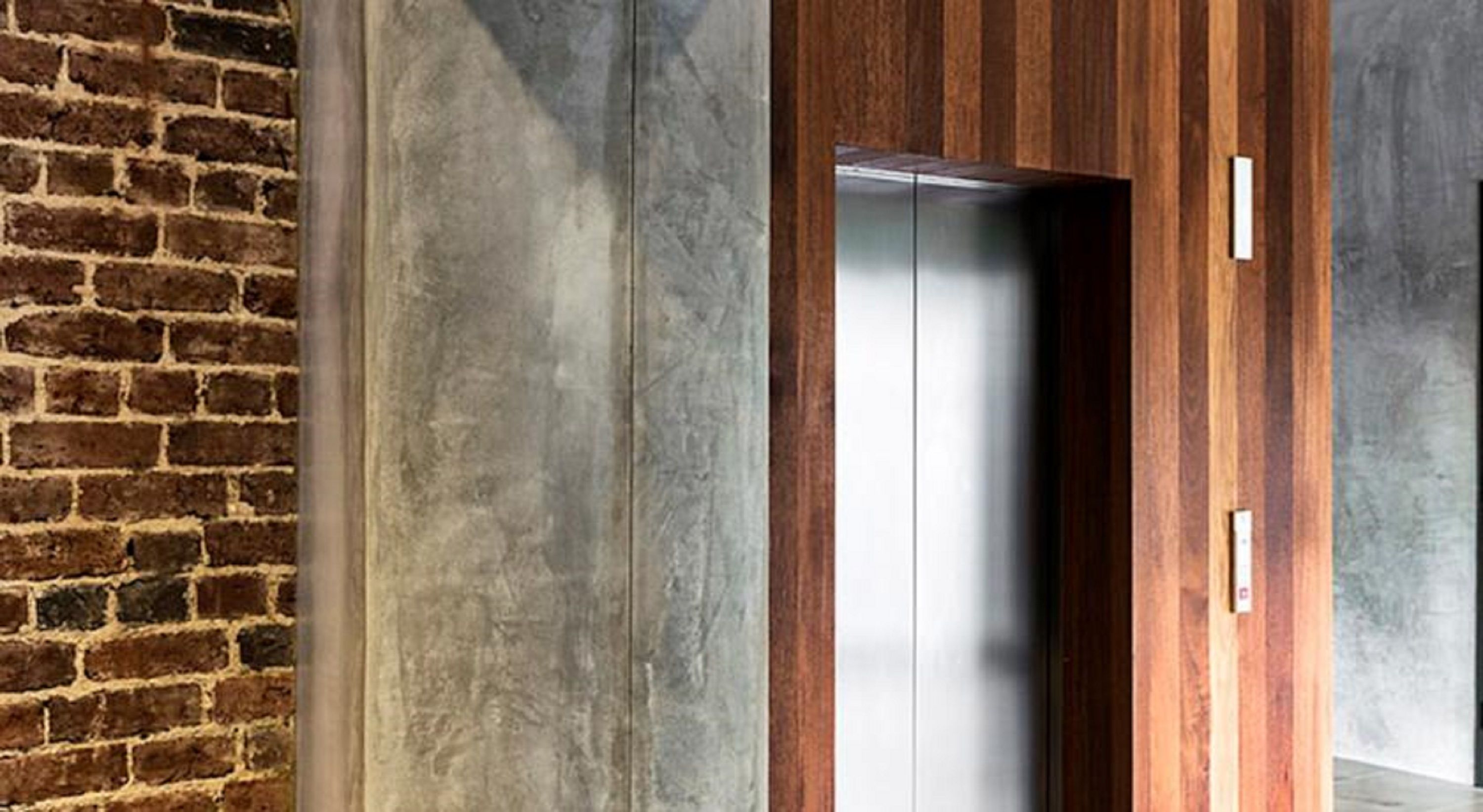 A modern elevator with a metallic finish, adjacent to a brick wall and wooden paneling.