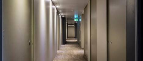 Un pasillo largo y estrecho con puertas a ambos lados, que conduce a una salida luminosa al final.