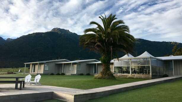 Un resort con varias cabañas, una palmera y montañas al fondo.