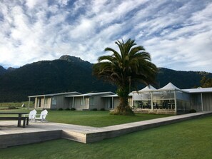 A resort with multiple cabins, a palm tree, and mountains in the background. - Franz Josef Oasis (Franz Josef Glacier)