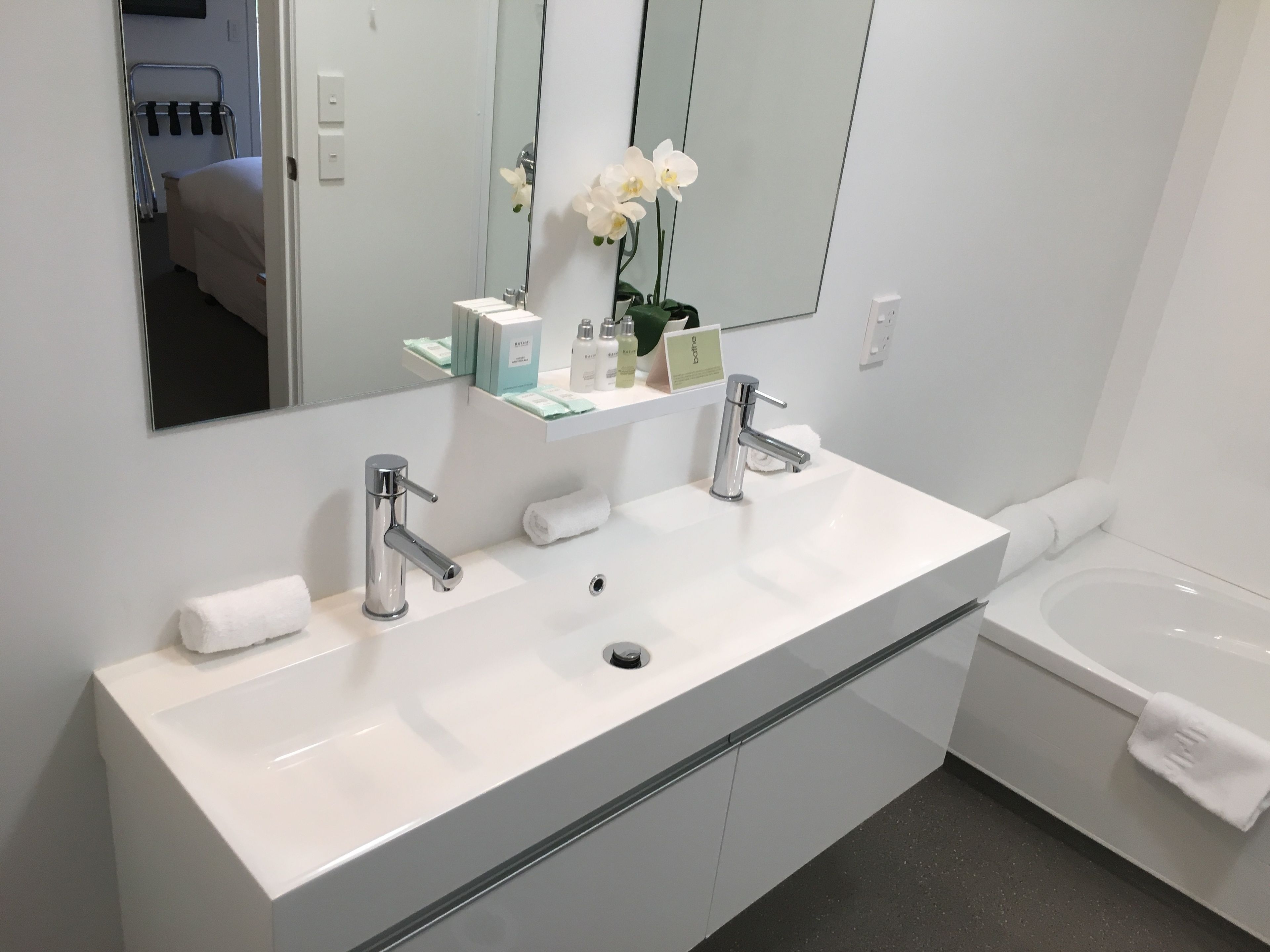 A modern bathroom with a white sink, two faucets, a mirror, and a bathtub.