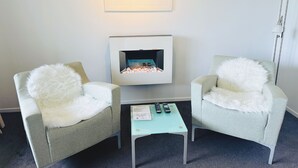 Una habitación moderna con dos sillones, una mesita, una chimenea y un cuadro en la pared.