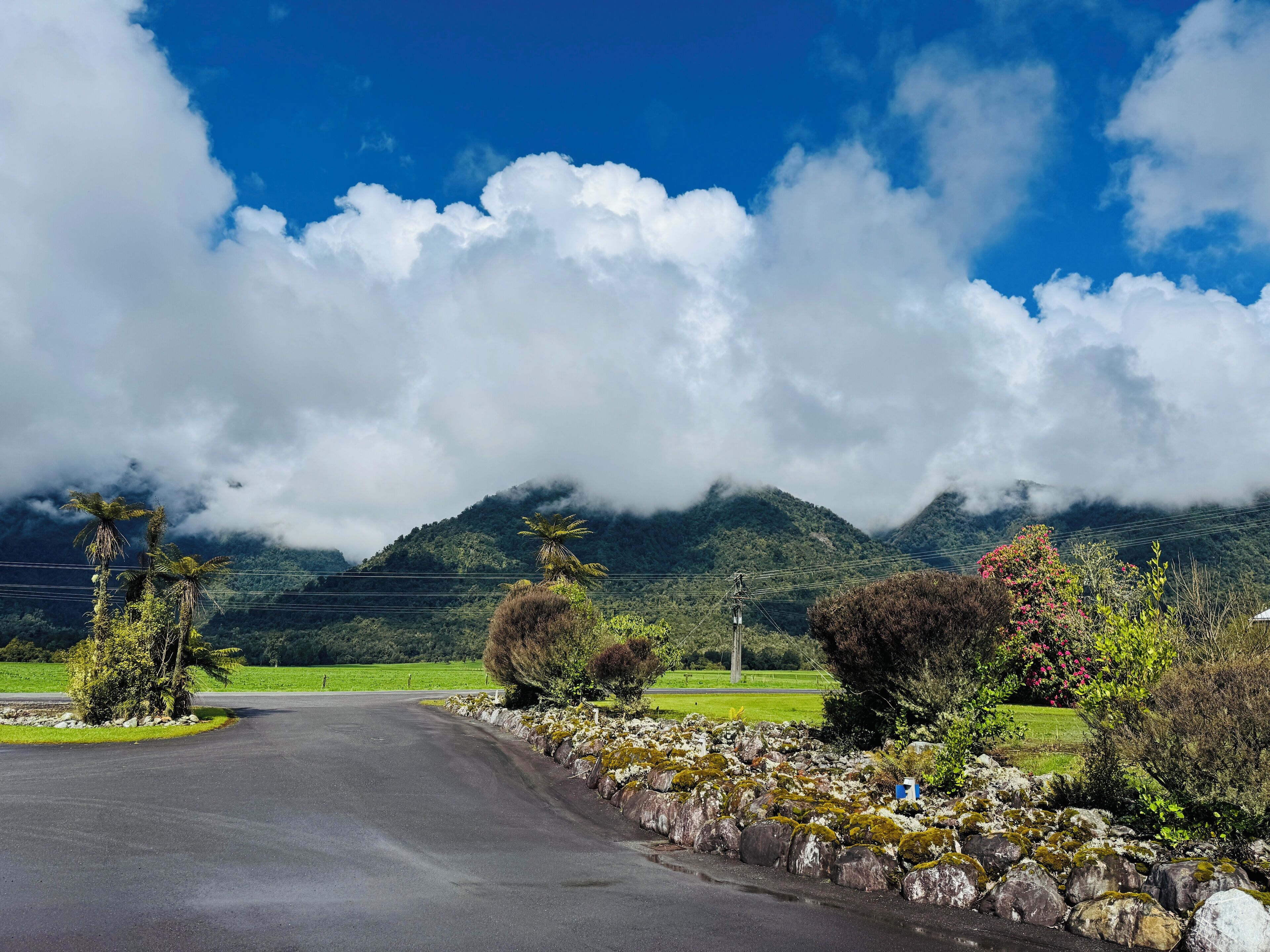 A rural road curving through a landscape with mountains and greenery.