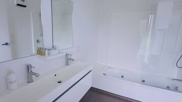 Un baño moderno con un lavamanos blanco, un espejo grande y una bañera.