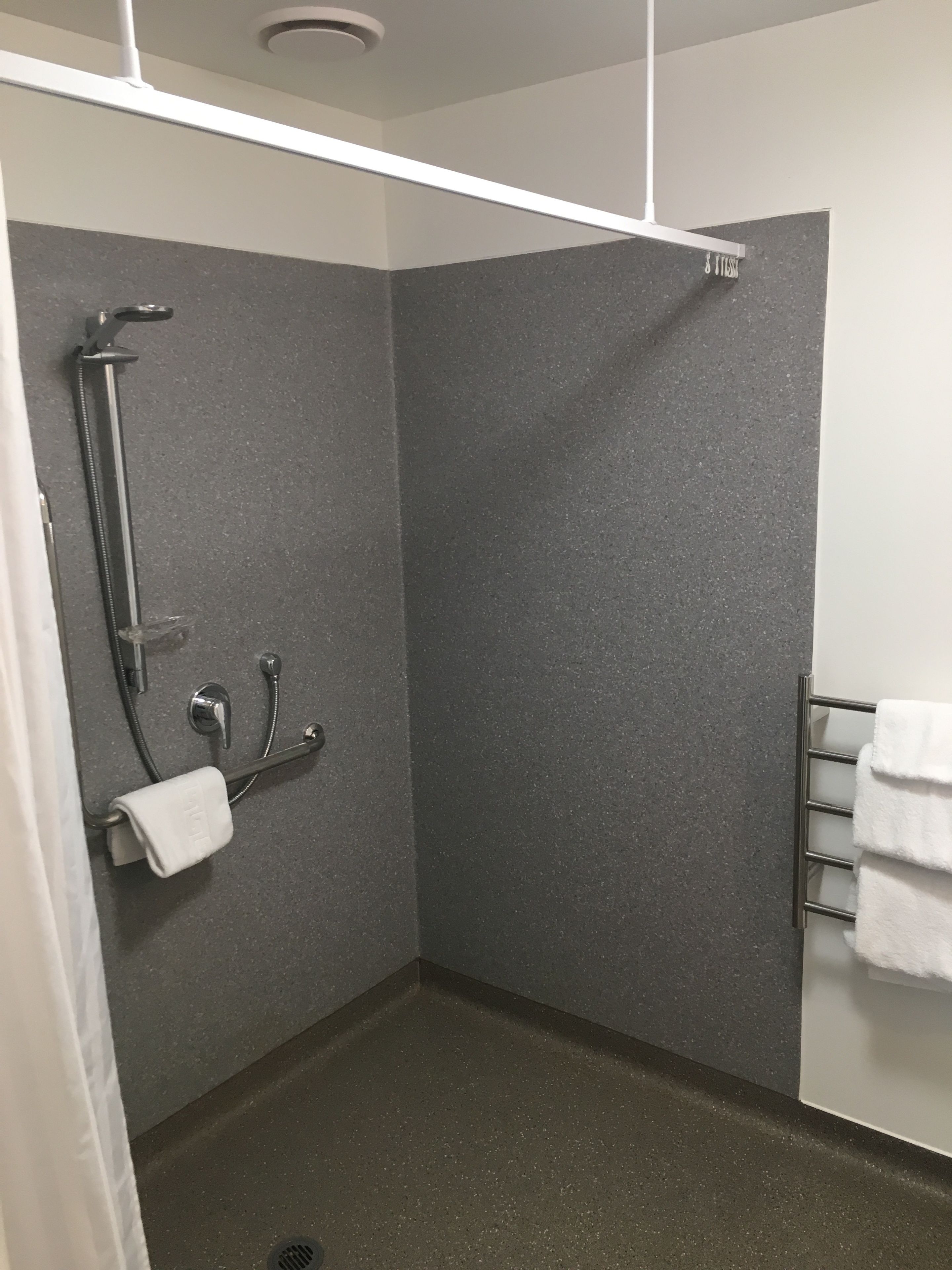 A modern shower area with a handheld showerhead, a wall-mounted faucet, and a towel rack with folded towels.