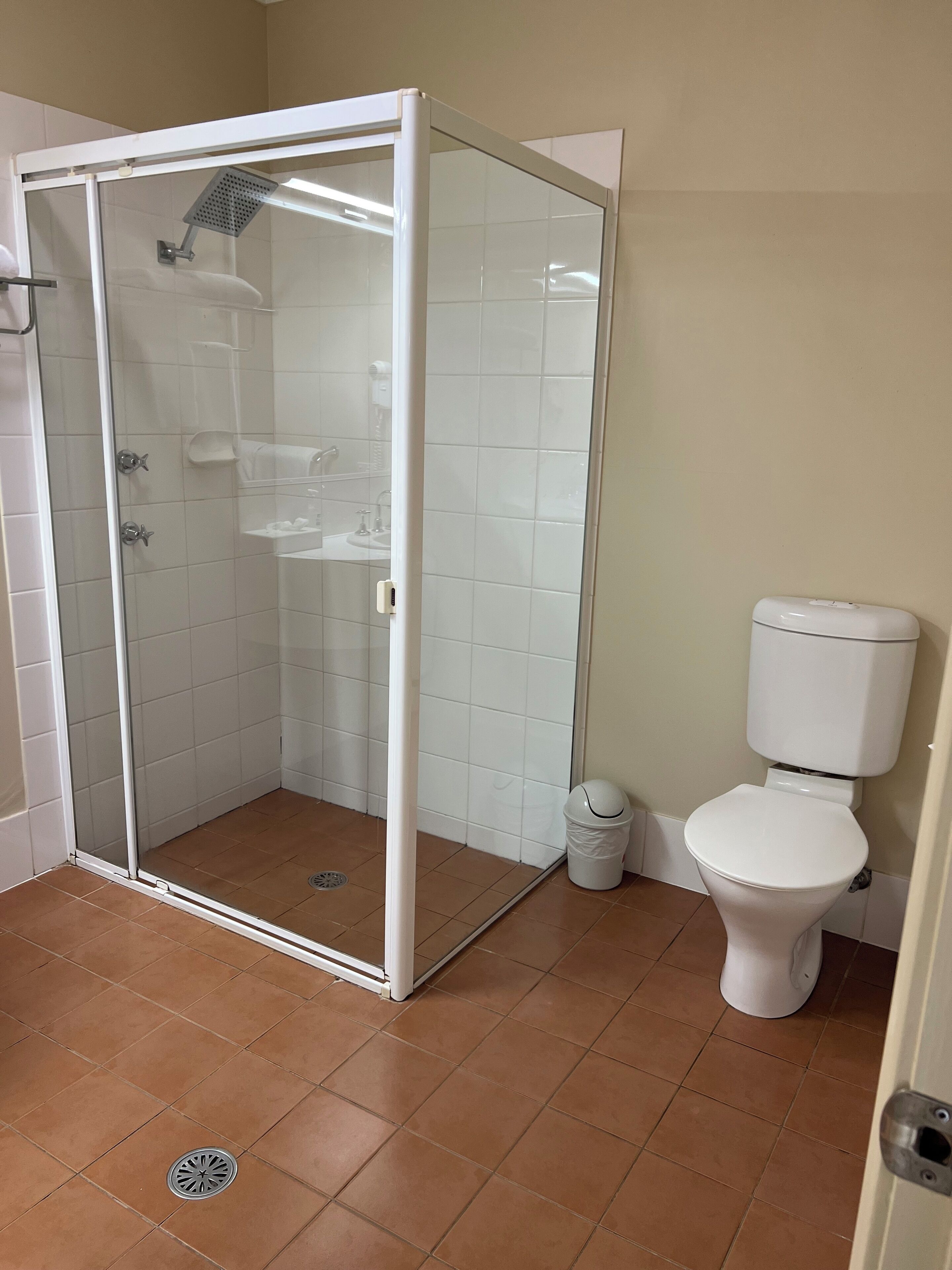 A bathroom with a glass-enclosed shower, a toilet, and a trash bin.