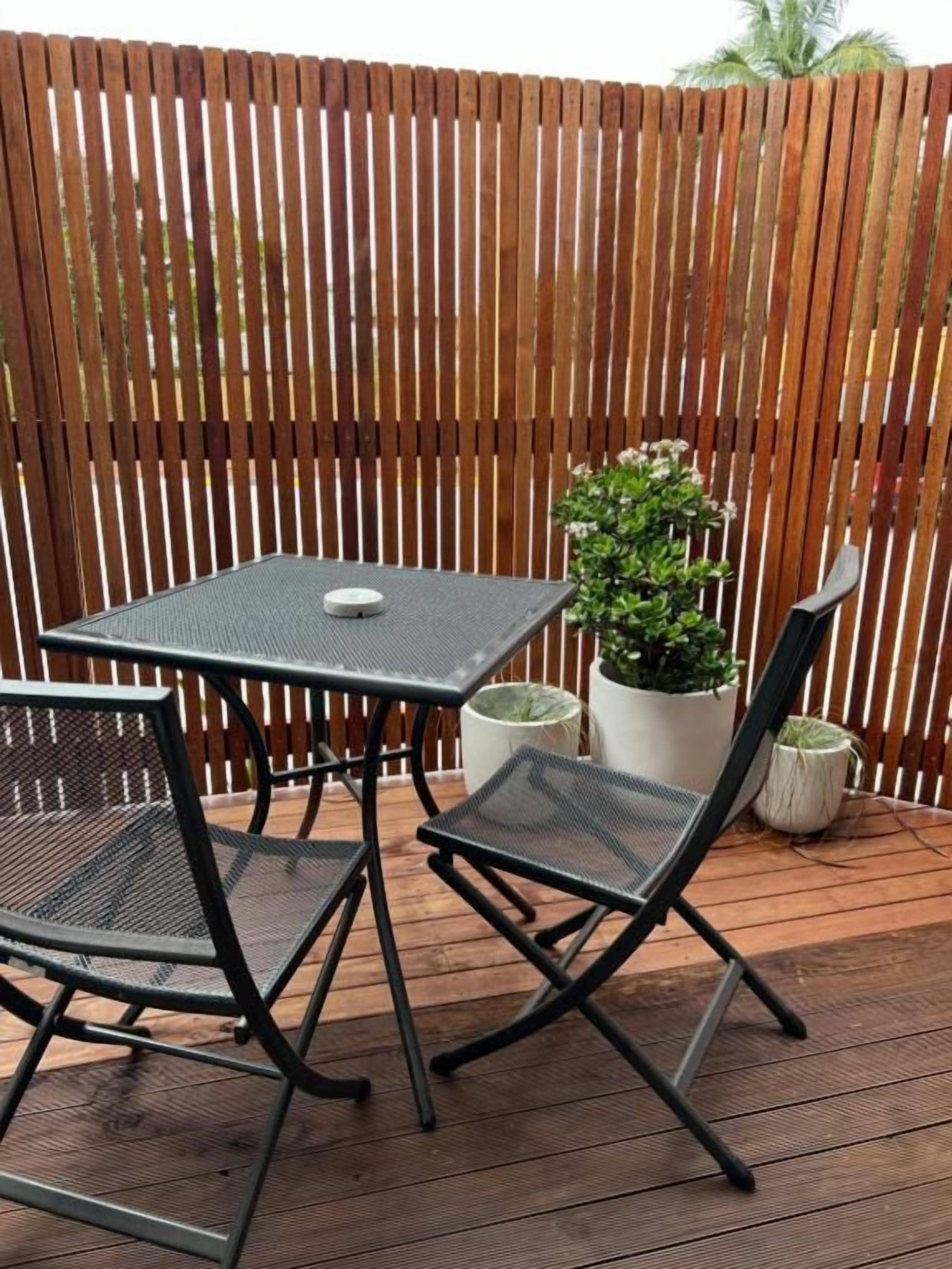 A wooden deck with a metal table and chairs, a potted plant, and a wooden fence.