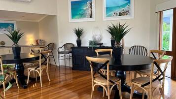 A dining area with a round table and chairs, a kitchen in the background, and two framed pictures on the wall.