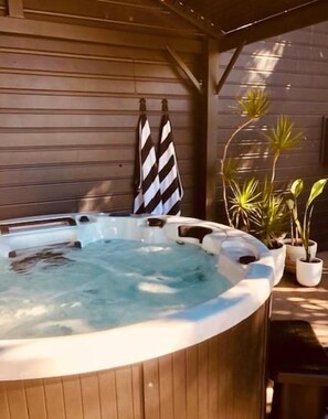 A hot tub with a wooden exterior, two towels hanging on a rack, and potted plants nearby. - Arabella Garden Inn Motel (Wollongbar)