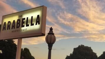 Schild für 'The Arabella North Coast' mit einer Straßenlaterne und Bäumen im Hintergrund.