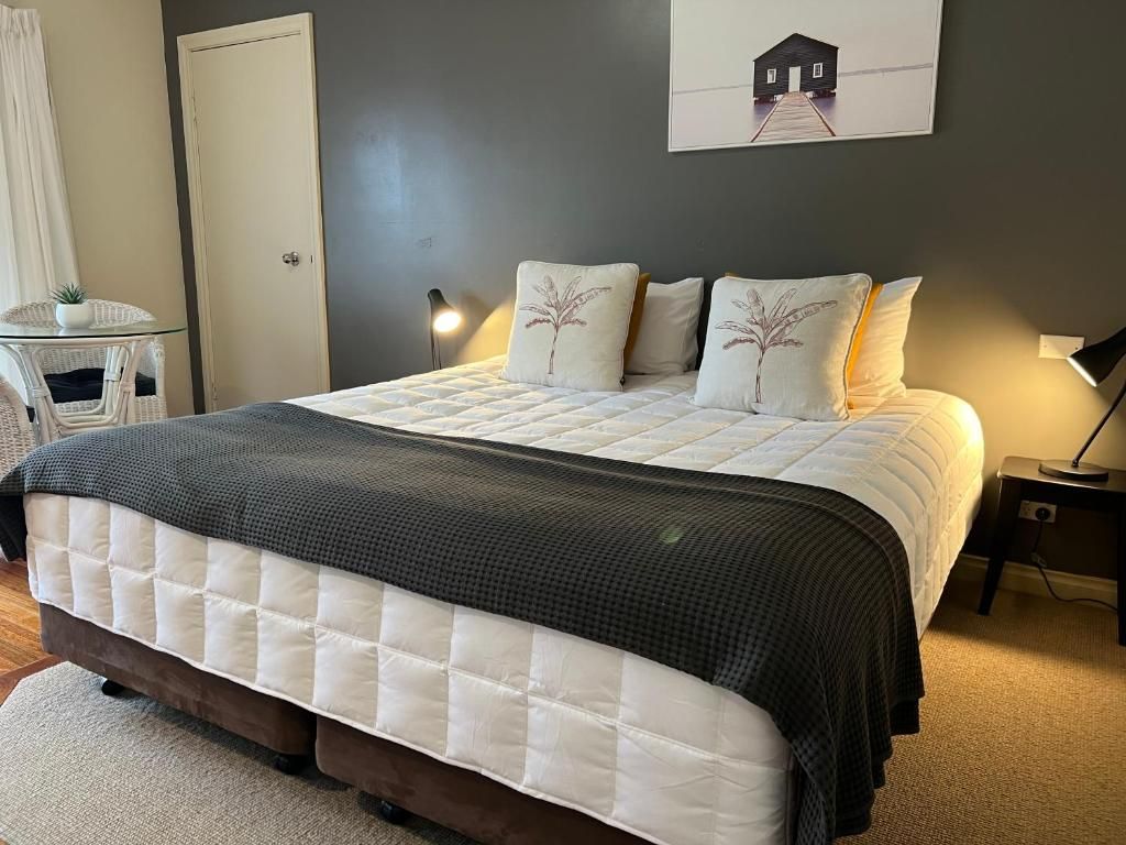 A bedroom with a bed, pillows, a bedside table, a lamp, a chair, a small table with a plant, and a door.