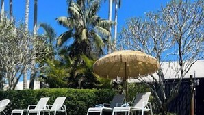 A pool with white lounge chairs and a straw umbrella. - Arabella Garden Inn Motel (Wollongbar)