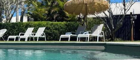 Ein Pool mit weißen Liegestühlen und einem Strohdachschirm.