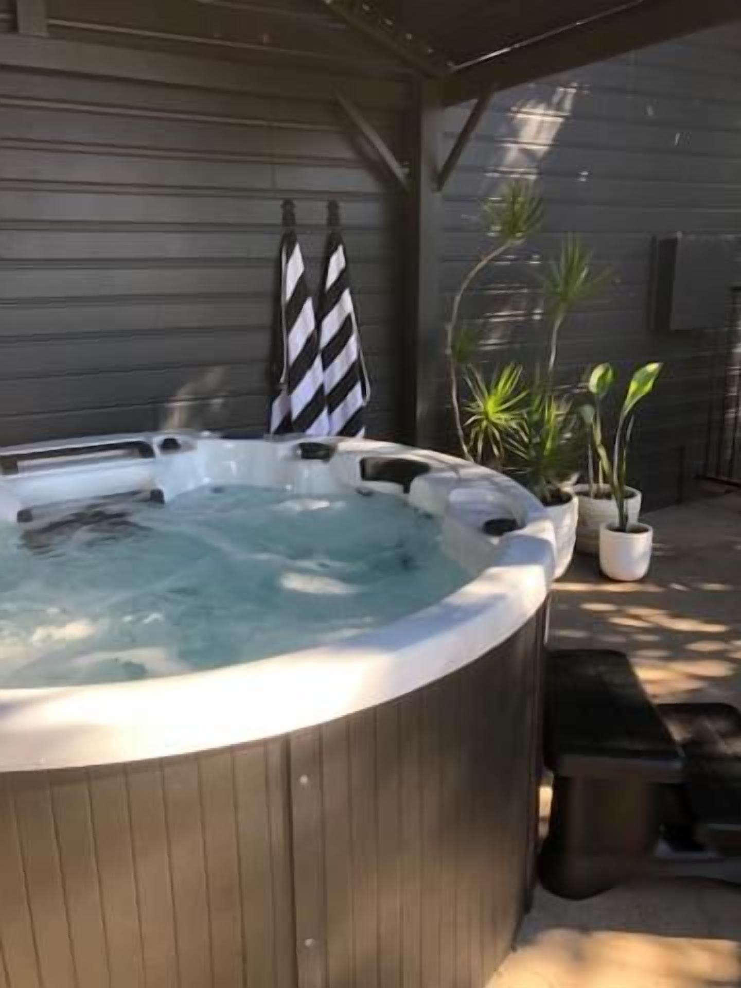 A hot tub in an outdoor setting with a wooden deck and potted plants.